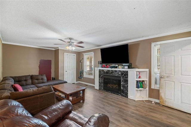 living room featuring a fireplace, wood-type flooring, ceiling fan, crown molding, and a textured ceiling