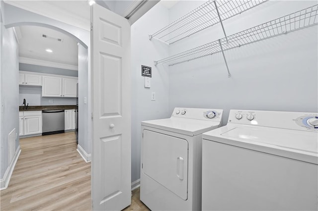 clothes washing area featuring light wood-type flooring, crown molding, sink, and washing machine and clothes dryer