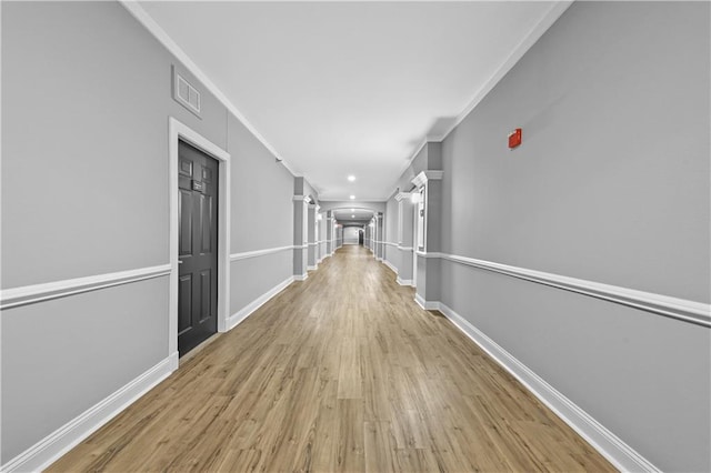 hallway featuring light wood-type flooring and decorative columns