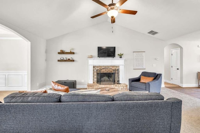 living room featuring a ceiling fan, arched walkways, a brick fireplace, lofted ceiling, and baseboards