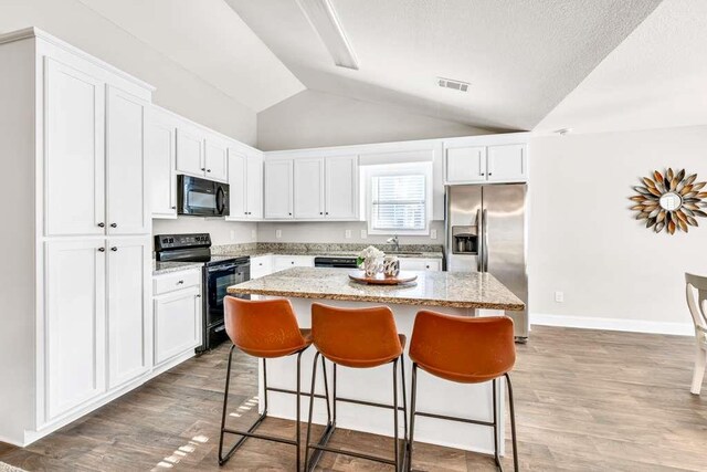 kitchen with black appliances, a kitchen island, white cabinets, a breakfast bar area, and lofted ceiling