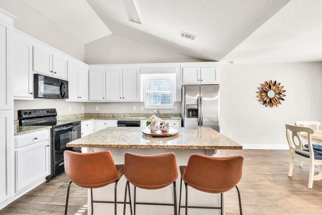 kitchen with black appliances, a kitchen island, a kitchen breakfast bar, white cabinetry, and vaulted ceiling