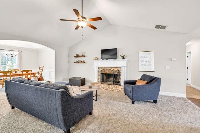 living area featuring arched walkways, a ceiling fan, a brick fireplace, carpet, and high vaulted ceiling
