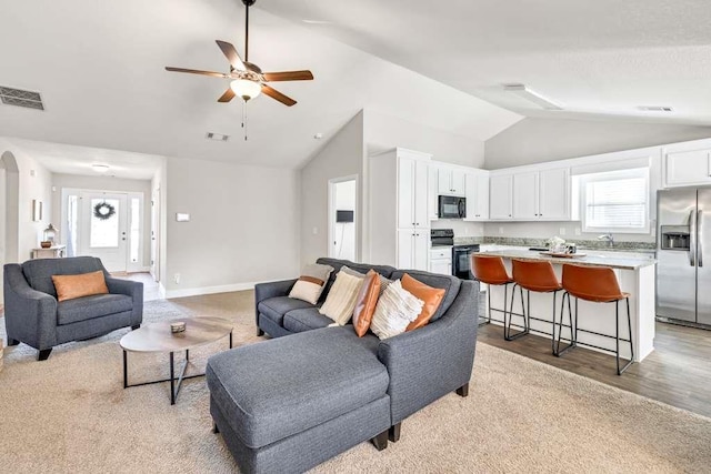 living room with healthy amount of natural light, vaulted ceiling, light wood finished floors, a ceiling fan, and baseboards