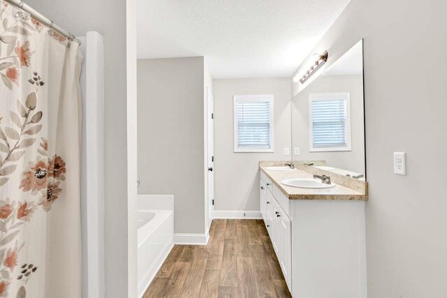 bathroom with wood finished floors, a garden tub, baseboards, double vanity, and a shower with curtain