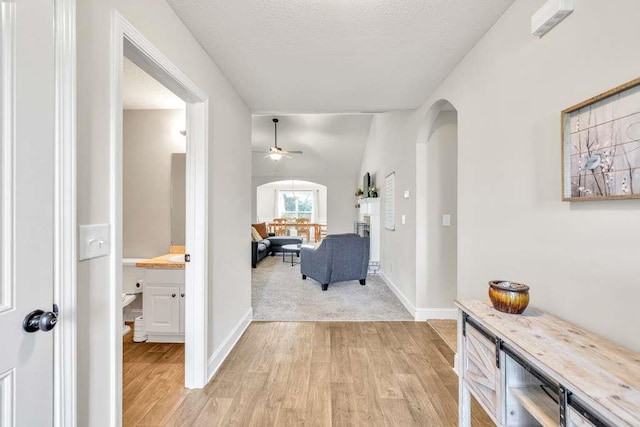 corridor featuring arched walkways, light wood finished floors, and baseboards