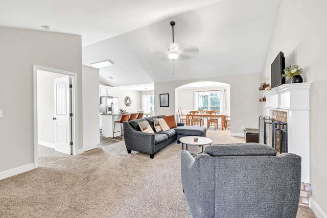 living room with vaulted ceiling, light carpet, ceiling fan, baseboards, and arched walkways