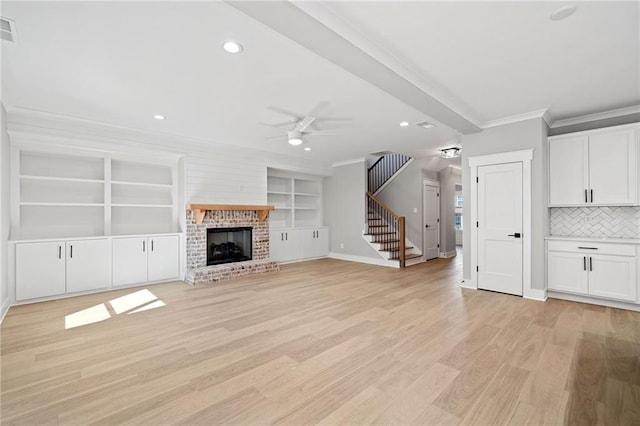 unfurnished living room with light wood-style flooring, stairway, ornamental molding, a brick fireplace, and ceiling fan