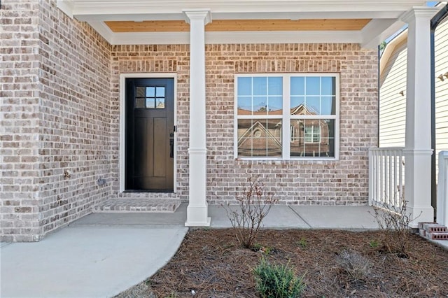 view of exterior entry featuring covered porch and brick siding