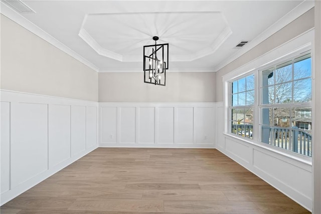 unfurnished dining area with light wood-style flooring, a decorative wall, visible vents, ornamental molding, and a tray ceiling