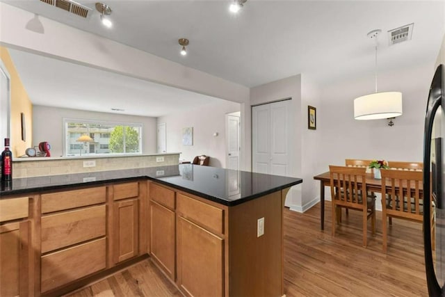 449 Clairemont Ave Unit H3, Decatur, GA 30030 - kitchen featuring light wood-style floors, a peninsula, hanging light fixtures, brown cabinetry, and dark stone counters