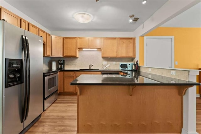 449 Clairemont Ave Unit H3, Decatur, GA 30030 - kitchen featuring appliances with stainless steel finishes, a breakfast bar, light wood-type flooring, dark countertops, and backsplash