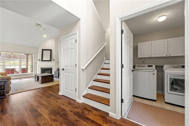 laundry area featuring cabinet space, dark wood-style flooring, washing machine and clothes dryer, a textured ceiling, and a fireplace