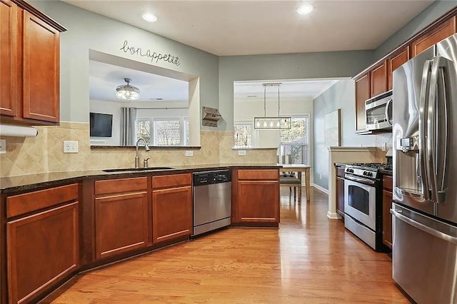 kitchen featuring appliances with stainless steel finishes, dark stone counters, sink, decorative light fixtures, and light hardwood / wood-style flooring