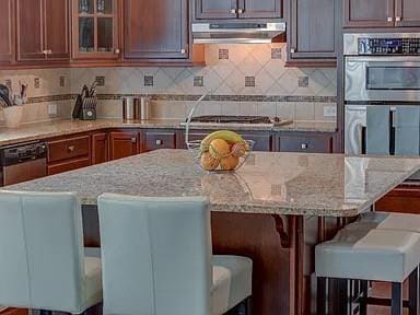 kitchen featuring light stone countertops, a breakfast bar area, backsplash, and appliances with stainless steel finishes