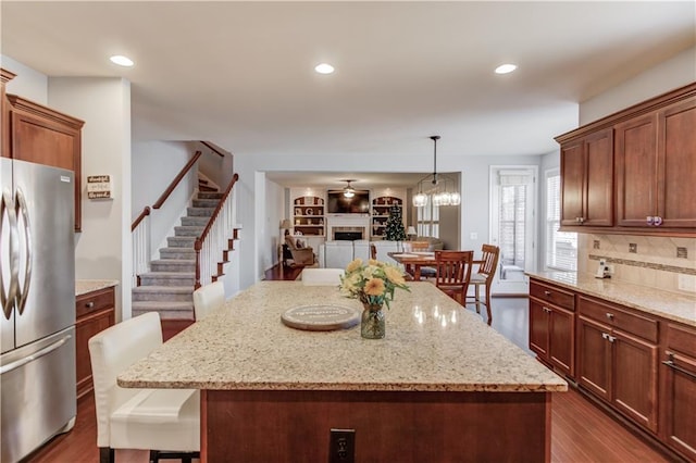 kitchen featuring light stone counters, decorative light fixtures, a center island, a kitchen breakfast bar, and stainless steel fridge