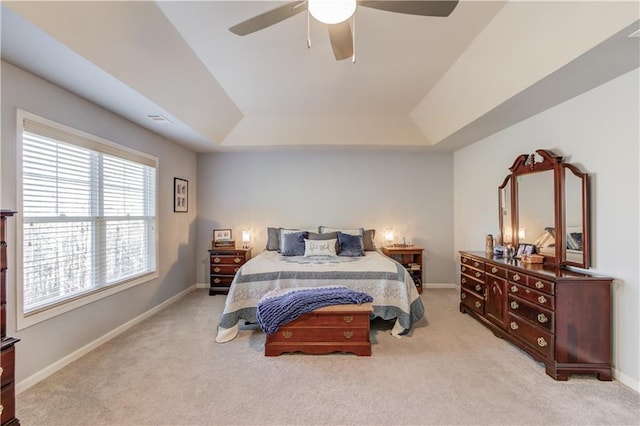 bedroom with ceiling fan, light colored carpet, and a tray ceiling