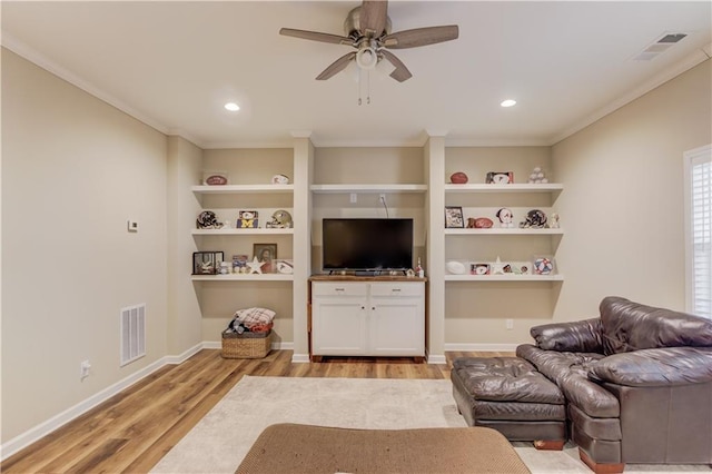 living room with crown molding, ceiling fan, light wood-type flooring, and built in shelves