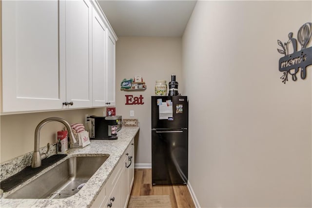 kitchen featuring black fridge, sink, light stone counters, and white cabinets