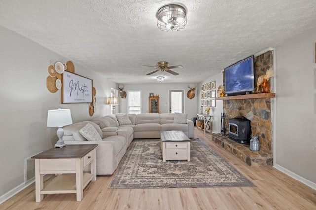 living room featuring ceiling fan, a wood stove, a textured ceiling, and light wood-type flooring