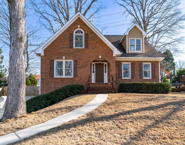 view of front of home with a shingled roof, a front yard, fence, and brick siding