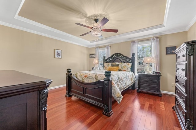 bedroom with a tray ceiling, dark wood-style flooring, ornamental molding, a ceiling fan, and baseboards