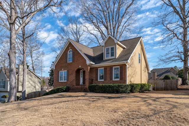 view of front of home with brick siding, a front lawn, a shingled roof, and fence