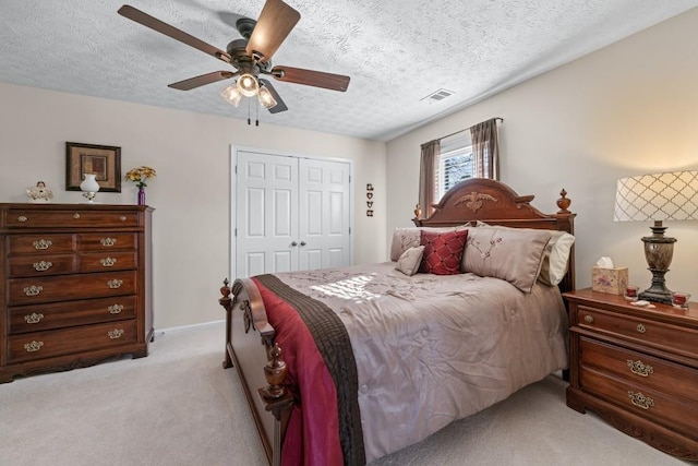 bedroom with light carpet, visible vents, a ceiling fan, a textured ceiling, and a closet