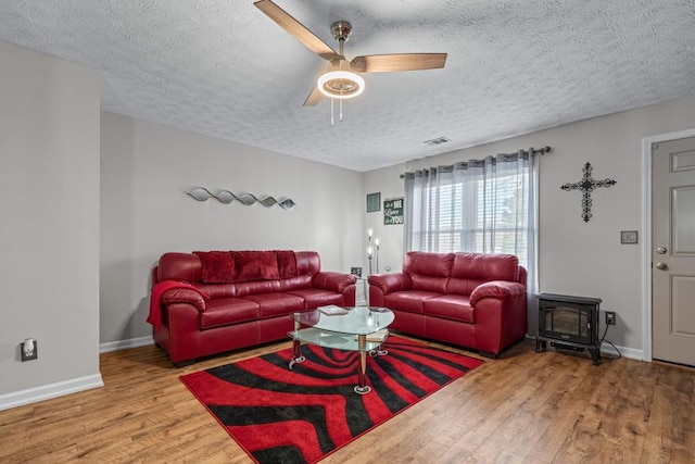 living room featuring visible vents, wood finished floors, a wood stove, and baseboards