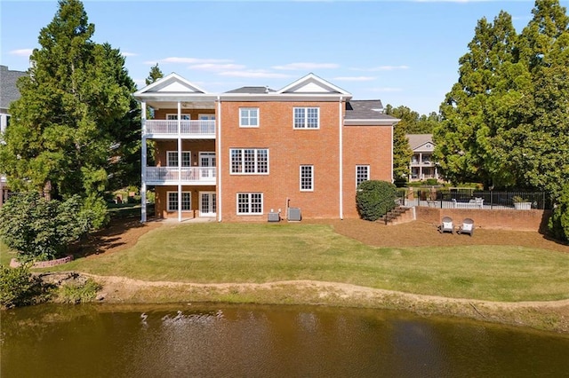 rear view of house with a balcony, central AC unit, a lawn, and a water view