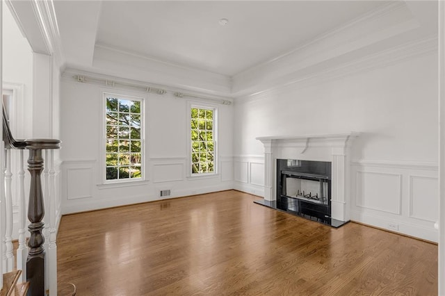 unfurnished living room featuring a high end fireplace, a raised ceiling, ornamental molding, and wood-type flooring