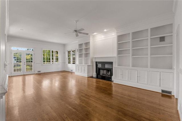 unfurnished living room featuring ceiling fan, french doors, ornamental molding, and built in shelves