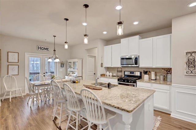 kitchen featuring stainless steel appliances, white cabinetry, a kitchen island with sink, and pendant lighting