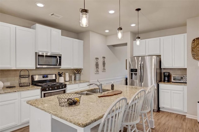 kitchen featuring appliances with stainless steel finishes, sink, white cabinets, pendant lighting, and an island with sink