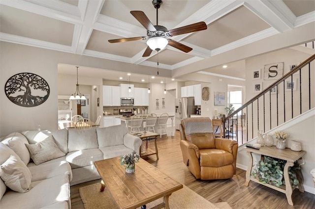 living room featuring crown molding, light hardwood / wood-style flooring, ceiling fan with notable chandelier, coffered ceiling, and beamed ceiling