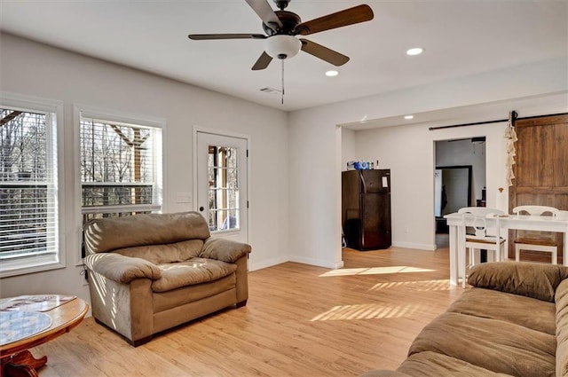 living room featuring light hardwood / wood-style floors, ceiling fan, and a barn door