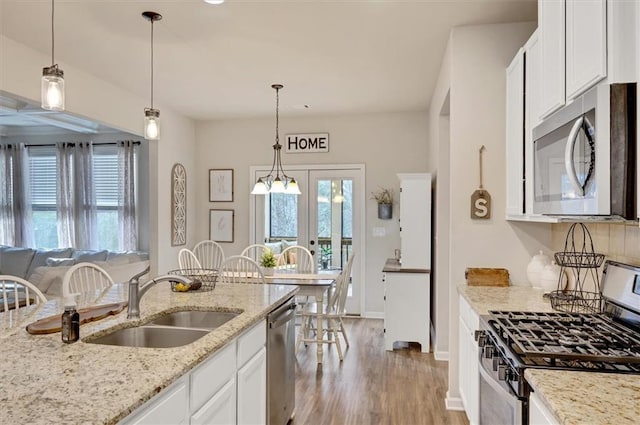 kitchen with light stone countertops, white cabinetry, sink, decorative light fixtures, and stainless steel appliances