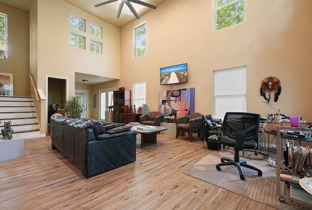 living area with a towering ceiling, light wood-style flooring, a ceiling fan, a desk, and stairway