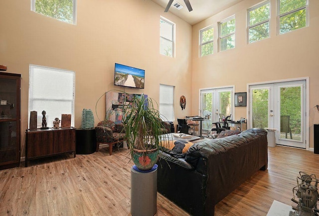living area with french doors, a towering ceiling, wood finished floors, and ceiling fan