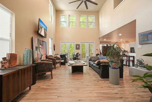 living room featuring ceiling fan, light wood-style flooring, a towering ceiling, french doors, and healthy amount of natural light