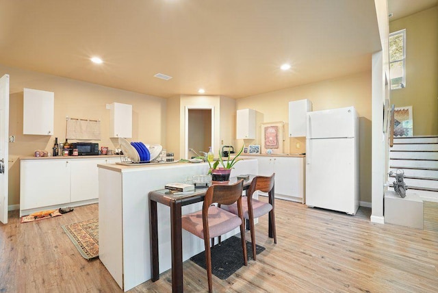 kitchen featuring freestanding refrigerator, white cabinets, black microwave, light wood finished floors, and recessed lighting