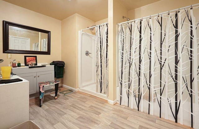 bathroom with wood finished floors, a shower with shower curtain, baseboards, and vanity