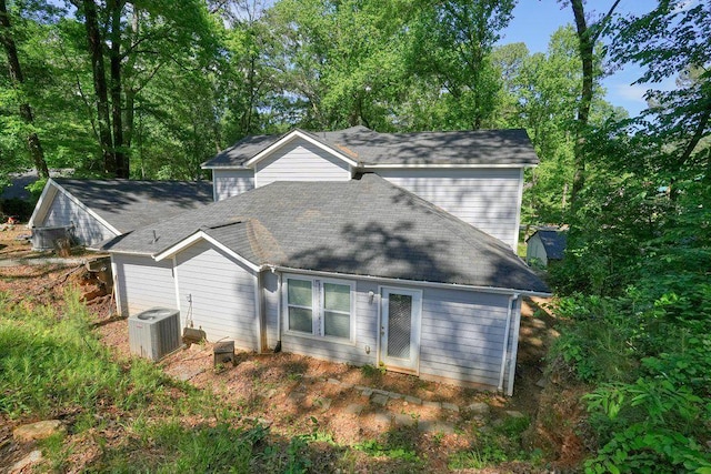 rear view of house with central AC unit and a shingled roof