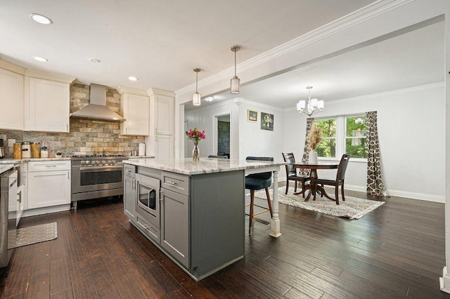 kitchen featuring wall chimney range hood, appliances with stainless steel finishes, gray cabinets, a kitchen breakfast bar, and baseboards
