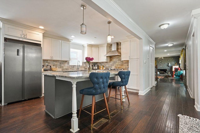kitchen featuring freestanding refrigerator, wall chimney exhaust hood, a center island, tasteful backsplash, and dark wood-type flooring