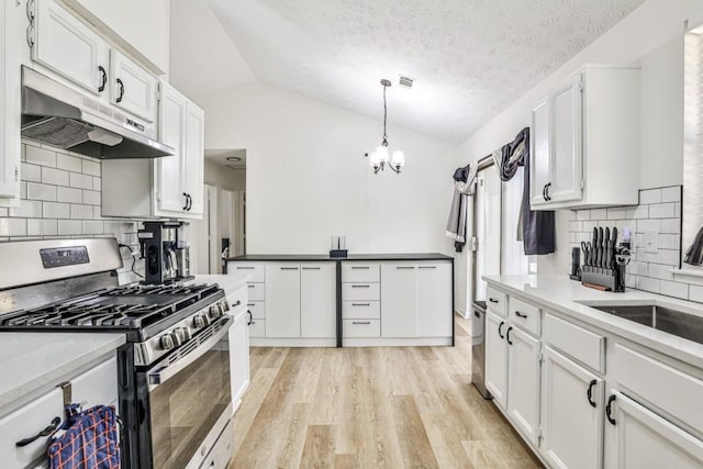 kitchen with light wood finished floors, stainless steel gas range, vaulted ceiling, white cabinets, and under cabinet range hood