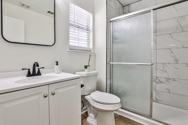 full bathroom featuring a shower with door, visible vents, toilet, and vanity