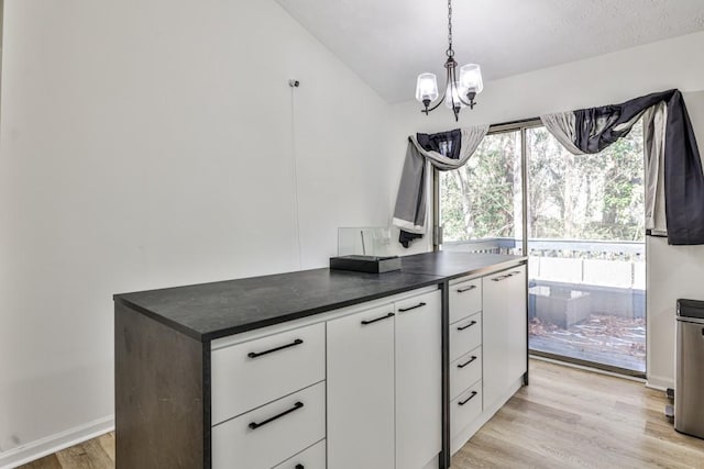 kitchen with an inviting chandelier, light wood-style flooring, hanging light fixtures, white cabinetry, and dark countertops