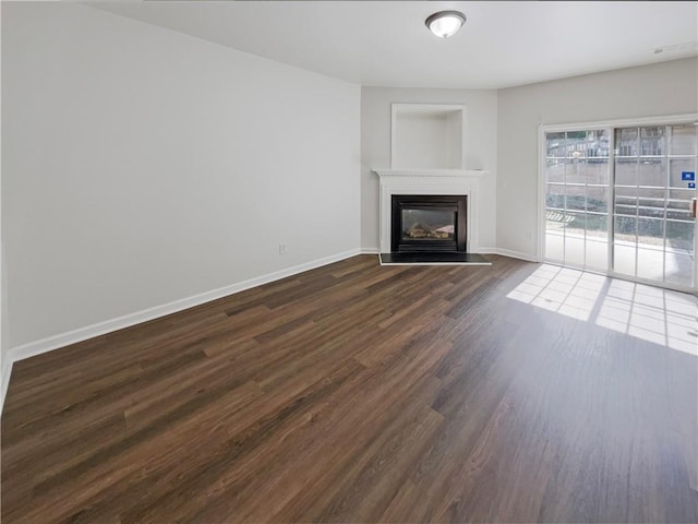 unfurnished living room featuring dark wood finished floors, a glass covered fireplace, and baseboards