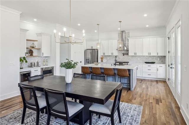 dining room featuring light wood finished floors, baseboards, wine cooler, crown molding, and recessed lighting